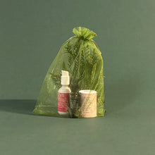 Load image into Gallery viewer, Green drawstring bag with skincare products on a green background
